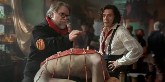 Guillermo del Tor stands on the Frankenstein set, examining a fake corpse with Oscar Isaac.