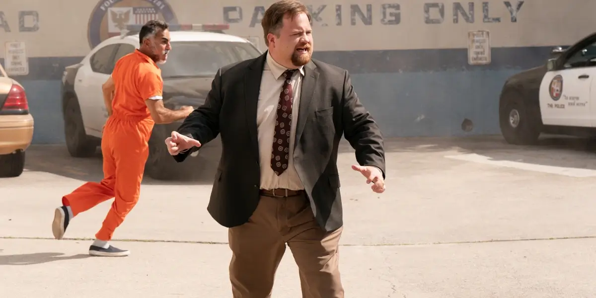 Paul Walter Hauser stands looking confused in the police station parking lot in The Naked Gun.