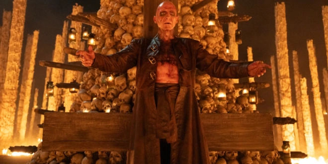 A made up Ralph Fiennes stands in front of a tower of skulls in 28 Years Later: The Bone Temple.