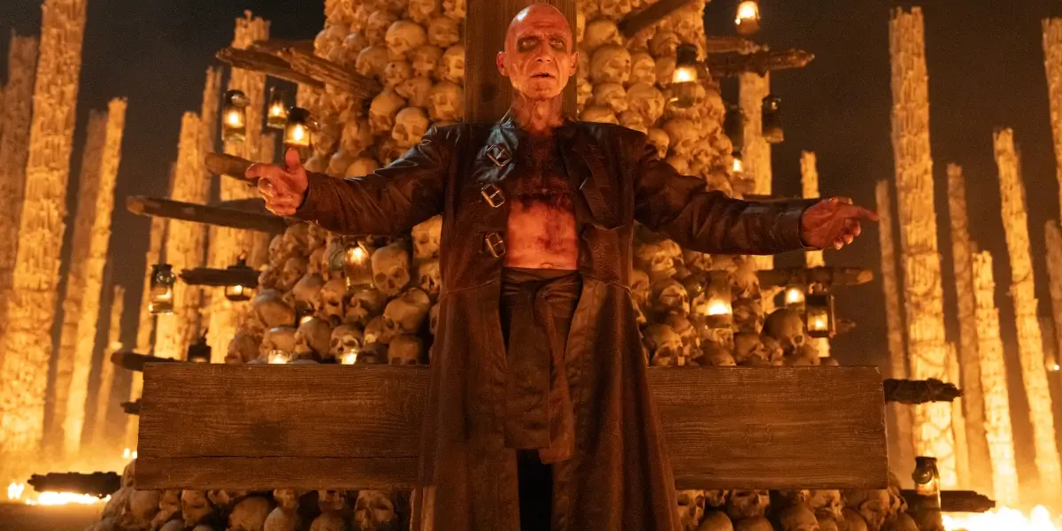 A made up Ralph Fiennes stands in front of a tower of skulls in 28 Years Later: The Bone Temple.