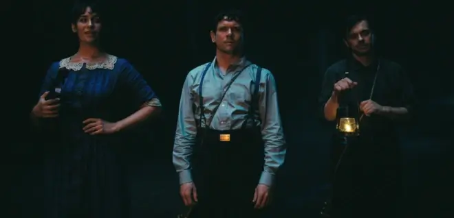 Lola Kirke, Jack O'Connell, and Peter Dreimanis stand ominously in the dark in Sinners.