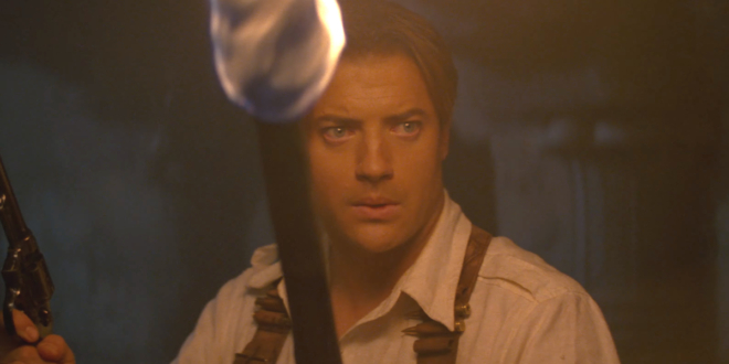 Brendan Fraser cautiously walks in a dark crypt with a gun and a torch in The Mummy Returns.