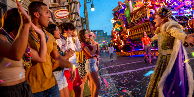 A crowd of excited parade watchers happily shout with the Queen of Mardi Gras at Universal Mardi Gras 2026.