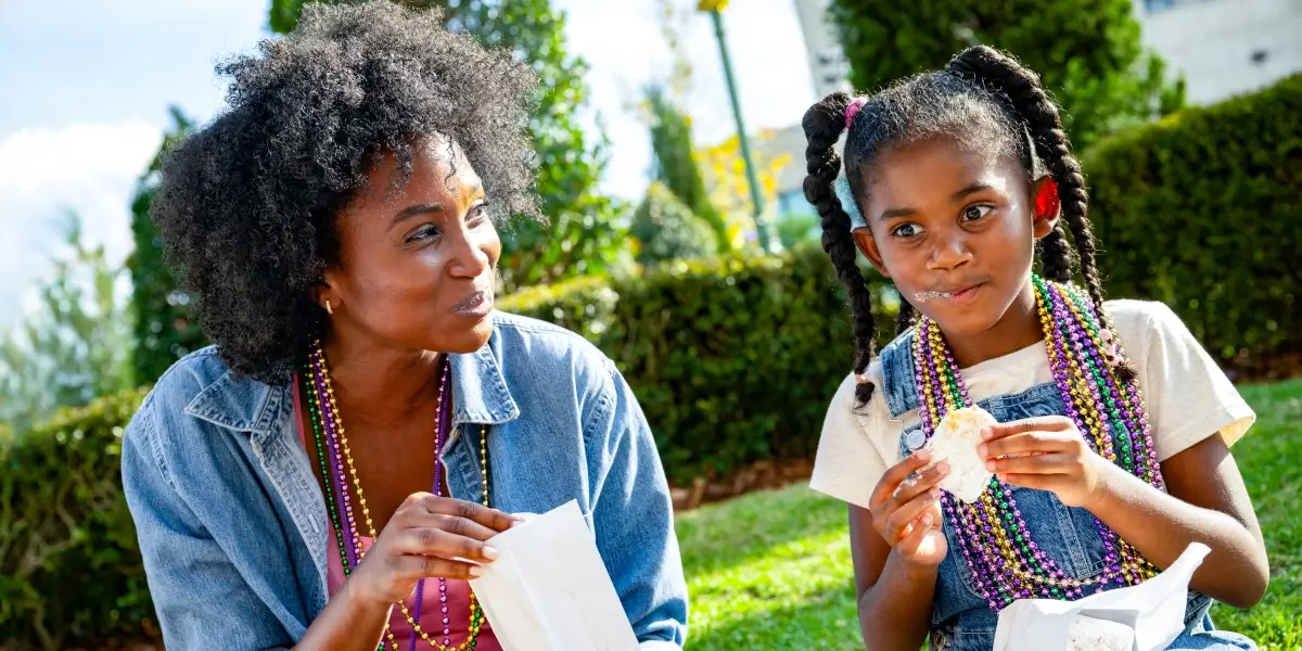 A mother and her daughter sit in a courtyard enjoying Beignets at Universal Mardi Gras 2026.