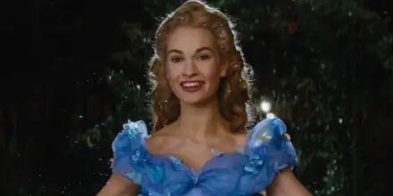 Lily James stands smiling in a blue dress crowded with butterflies in Cinderella (2015).