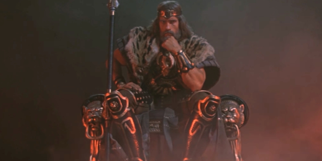 Arnold Schwarzenegger sits on a throne slumped in thought in Conan The Barbarian.