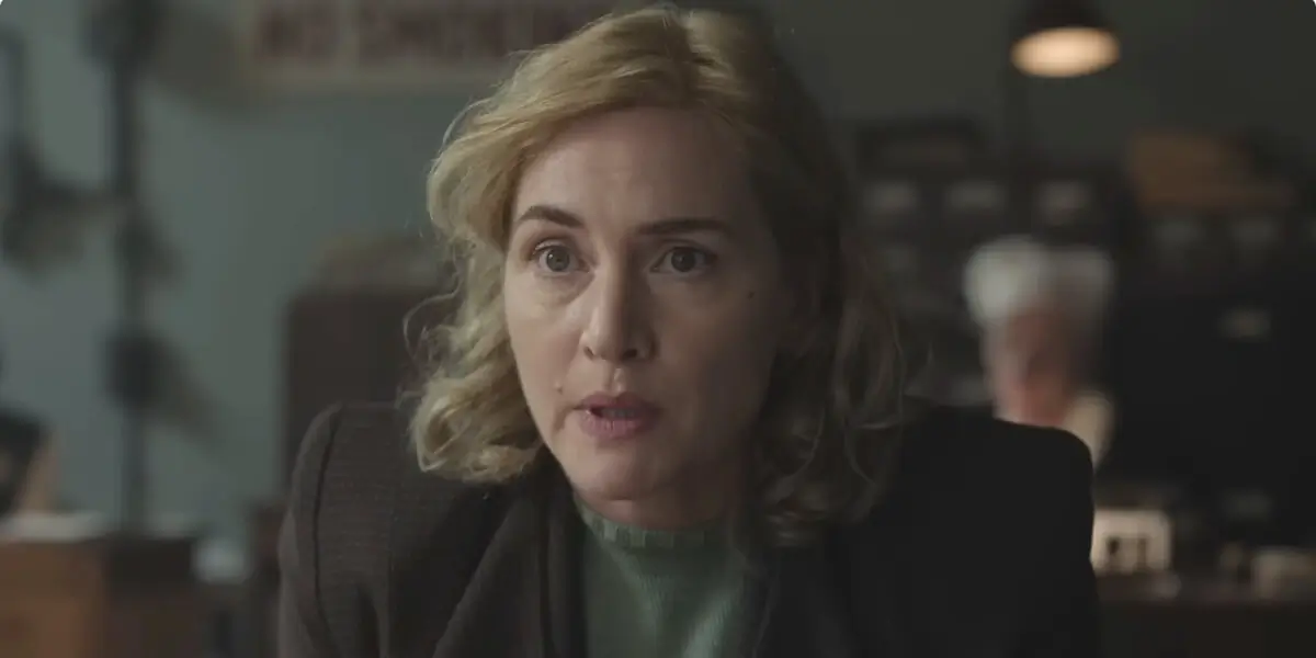 Kate Winslet leans over with urgency in an office in Lee.