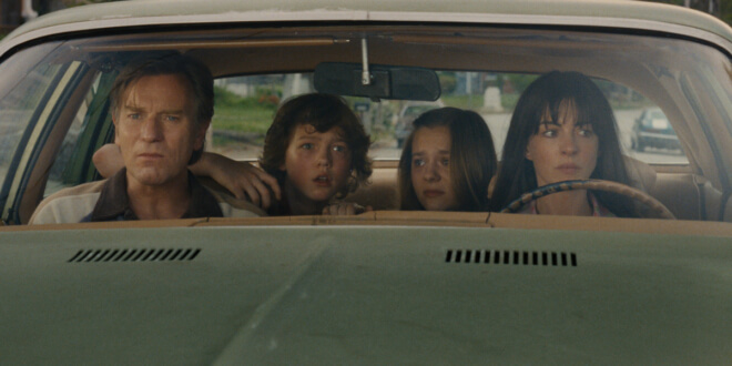Ewan McGregor and Anne Hathaway sit with their family in the car, looking around with fear and suspicion in The End of Oak Street.