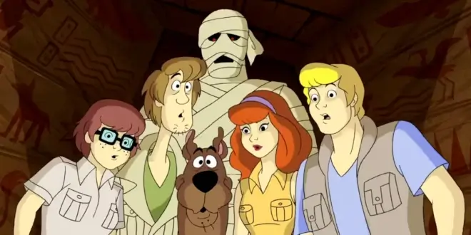 The Scooby Gang stands with curiosity while a mummy looms behind them in What's New Scooby Doo.