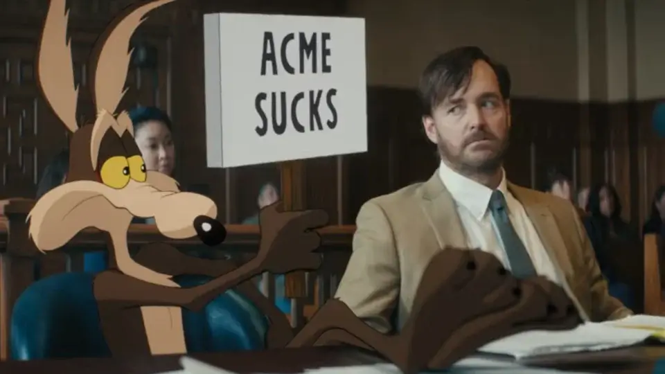 Wile E. Coyote holds up an anti ACME sign as Will Forte looks on with concern in Coyote vs. Acme.
