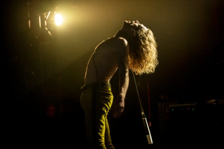 Sam Reid as the Vampire Lestat, head thrown back and lit by a single stage light.