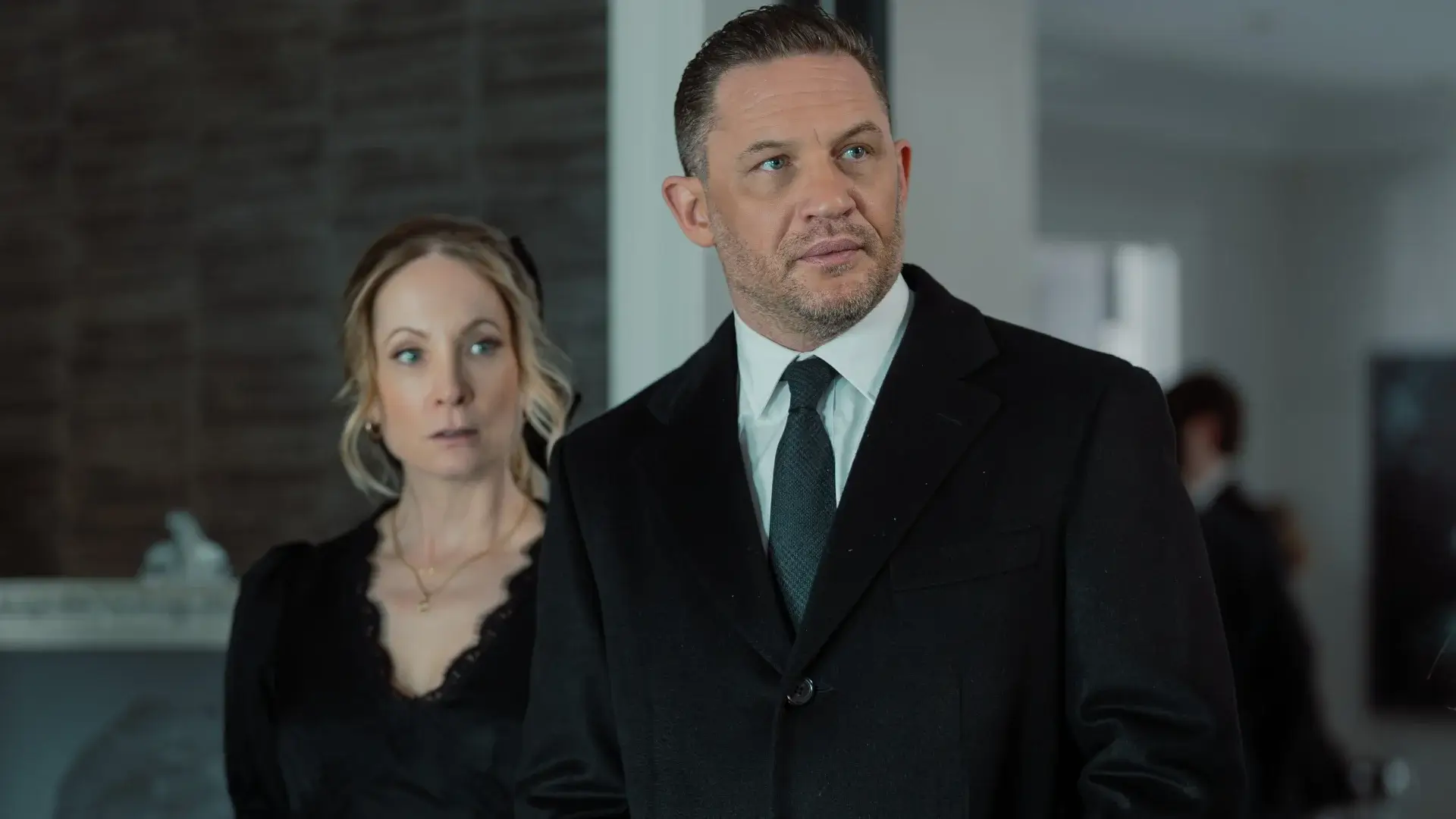A slightly shocked Joanne Froggatt stands next to a stern looking Tom Hardy at a funeral in MobLand S1 E5 - "Funeral for a Friend."