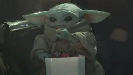 Grogu happily eats multicolored popcorn while at an event in The Mandalorian and Grogu,