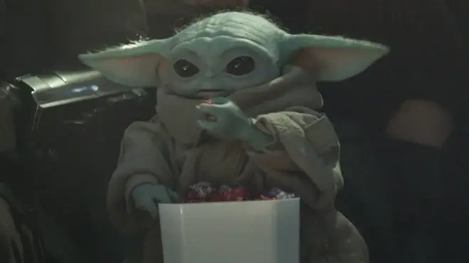 Grogu happily eats multicolored popcorn while at an event in The Mandalorian and Grogu,