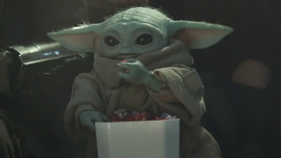 Grogu happily eats multicolored popcorn while at an event in The Mandalorian and Grogu,