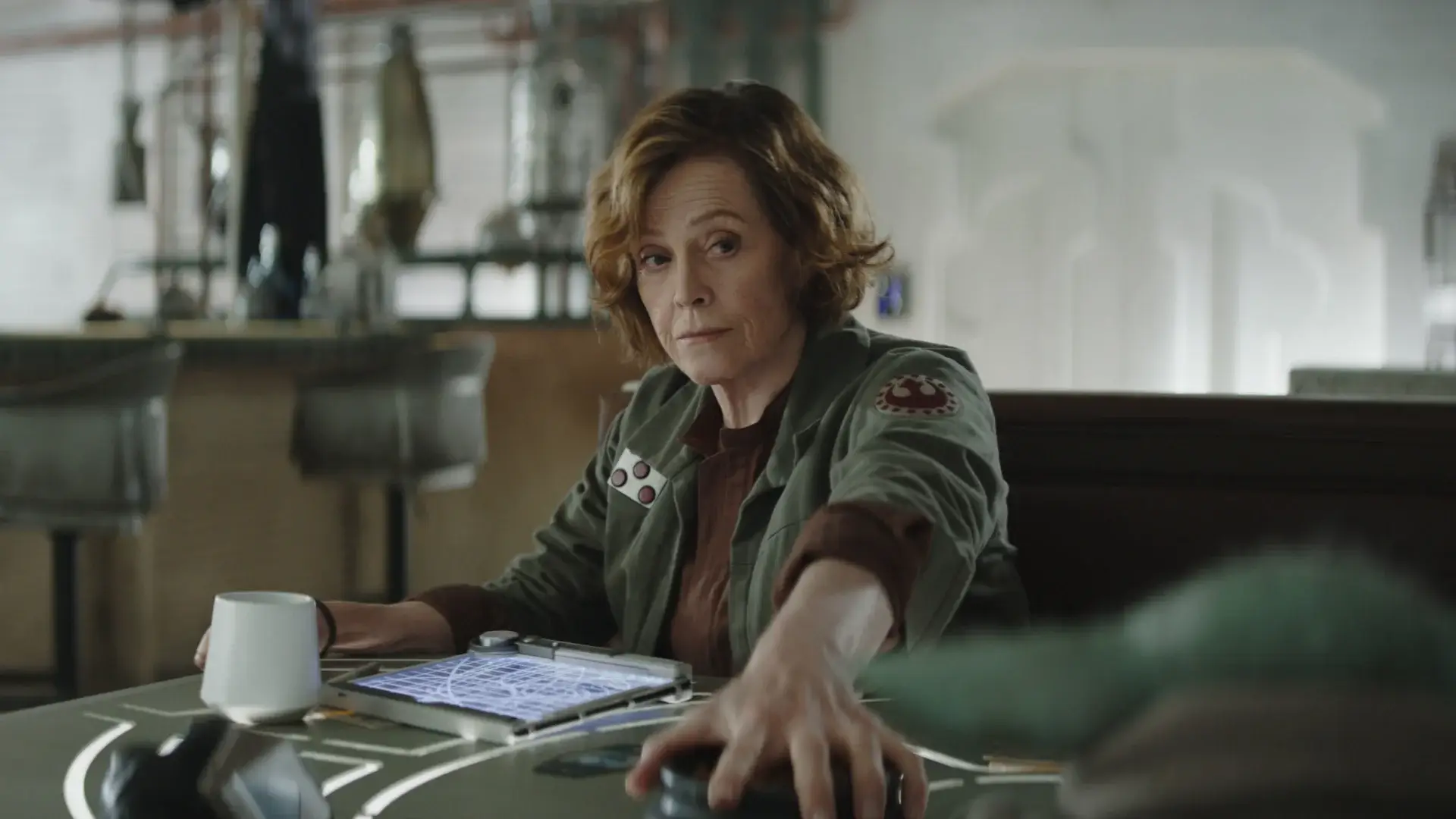 An annoyed Sigourney Weaver holds down a snack bowl in a cantina in The Mandalorian and Grogu.