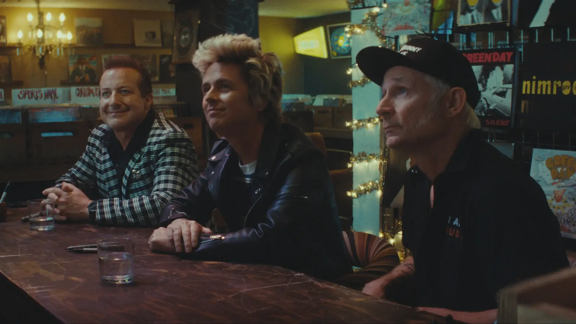 Tré Cool, Billie Joe Armstrong, and Mike Dirnt look up smiling while sitting at a signing table in Nimrods.