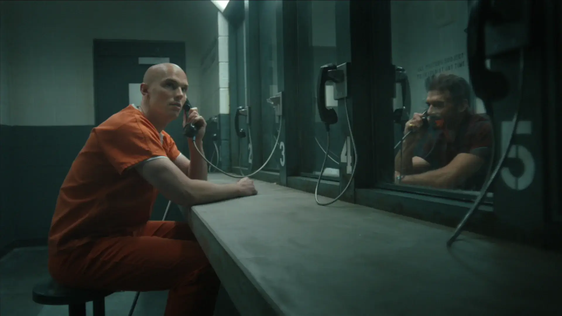 Nicholas Hoult sits on the prison phone with Frank Grillo on the other end in Peacemaker, Season 2 Episode 6 - "Ignorance is Chris."