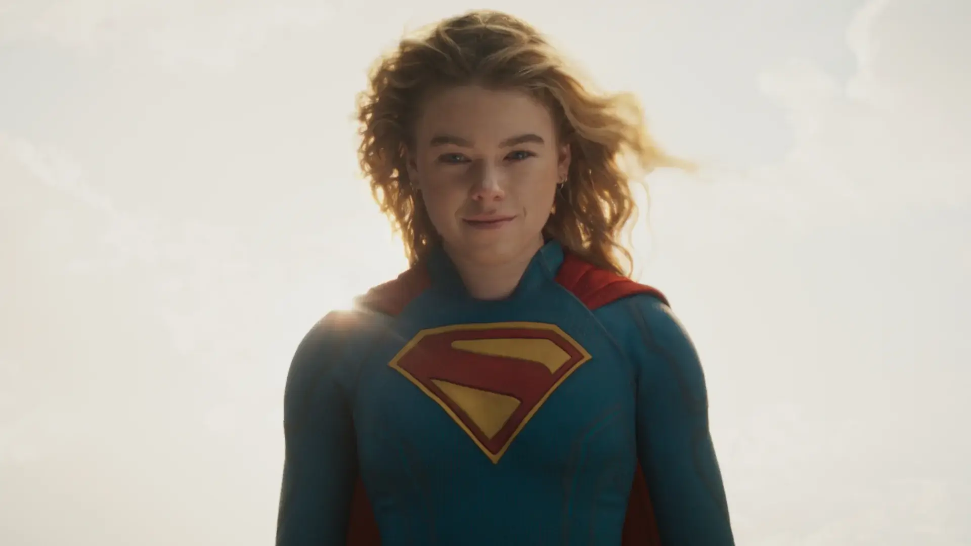A floating Milly Alcock smiles with the sun shining behind her in Supergirl.
