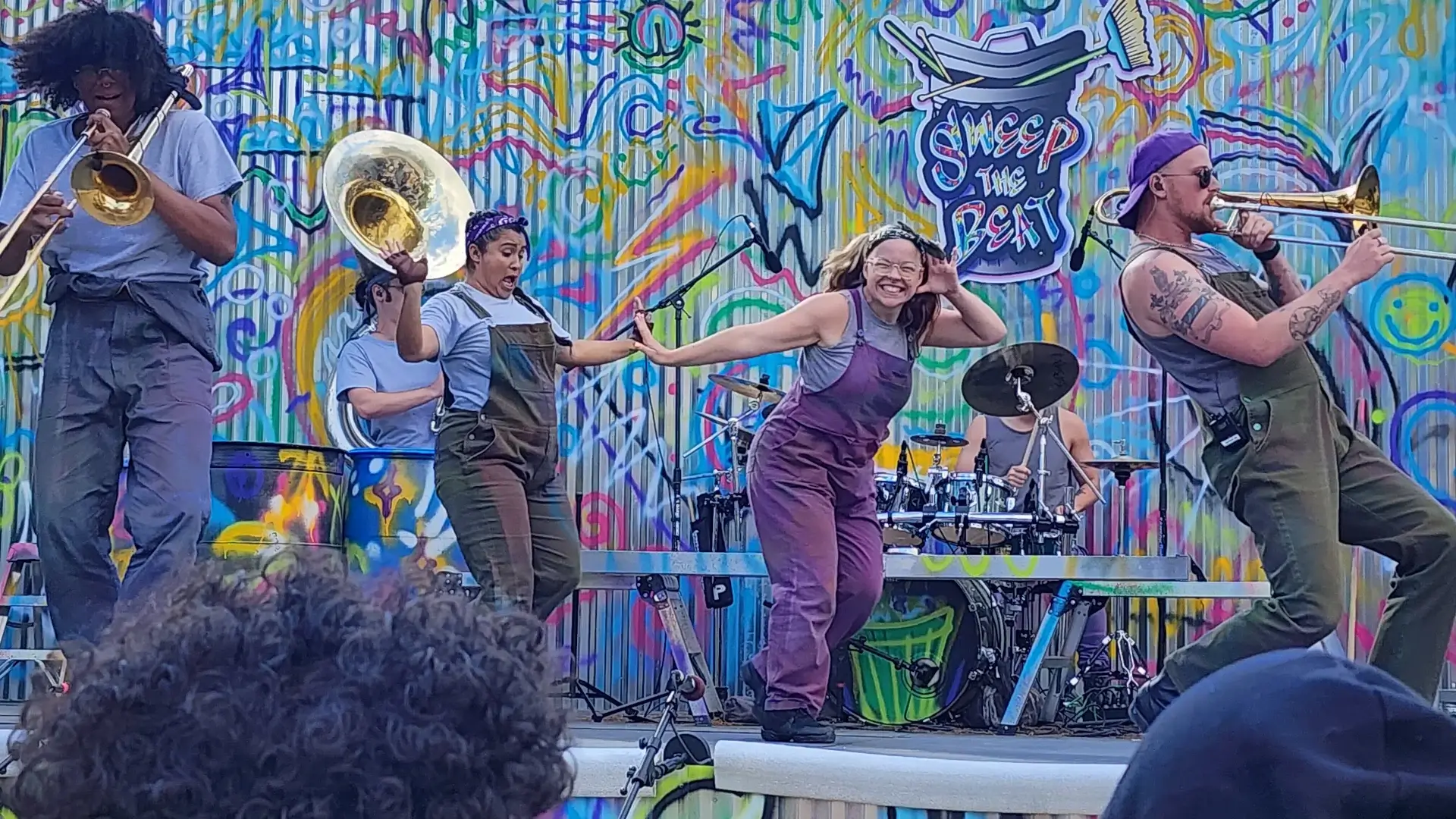 Sweep The Beat's dancers have fun on a colorful graffiti stage, while the band plays.