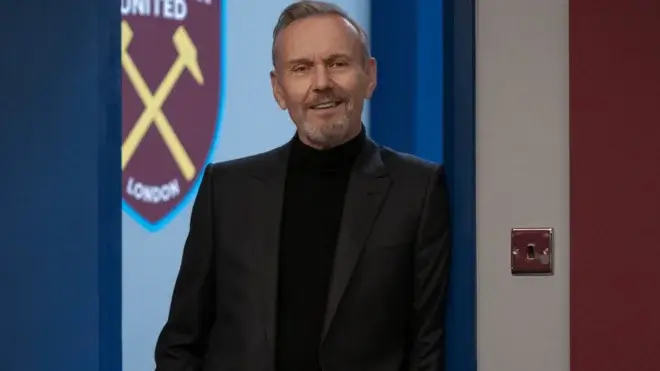 A bearded Anthony Stewart Head stands in a doorway with a smile in Ted Lasso, Season 3 Episode 4 - "Big Game."