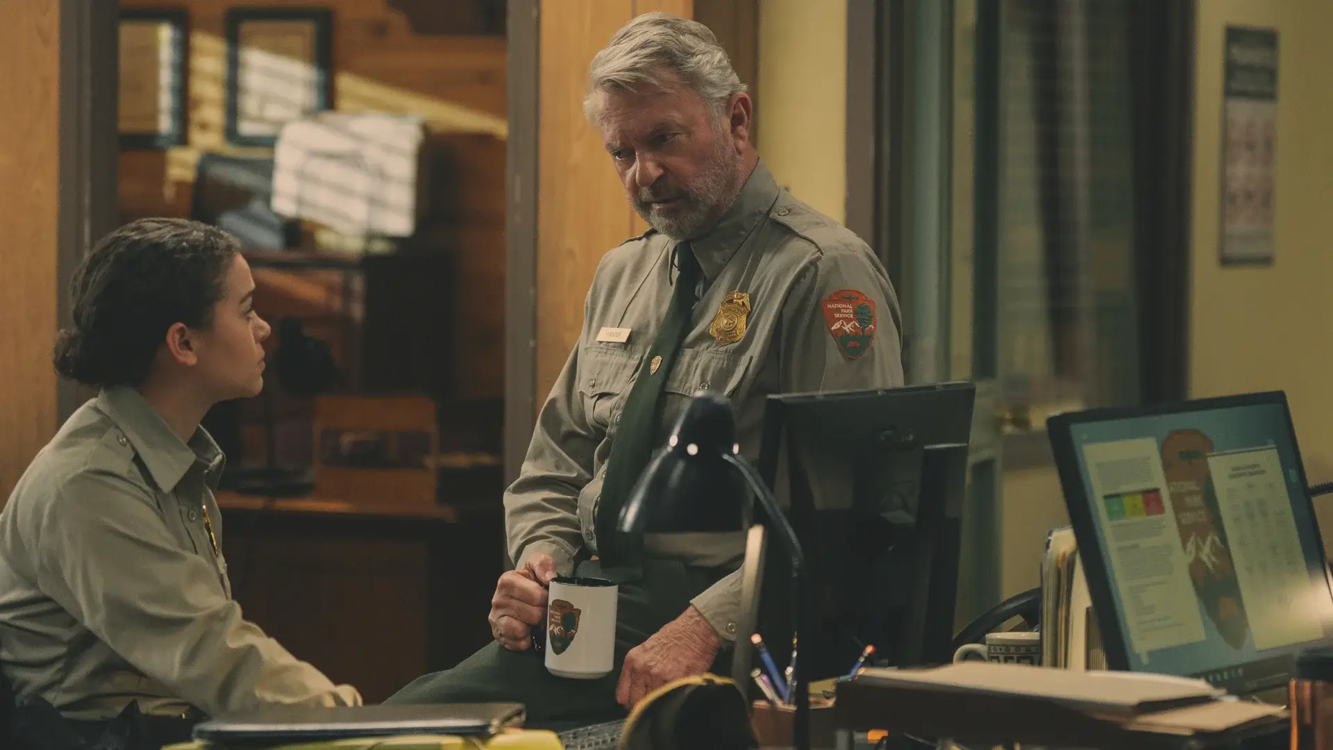 Lily Santiago looks up at Sam Neill as he sits on her desk in conversation in Untamed, Season 1 Episode 2 - "Jane Doe."