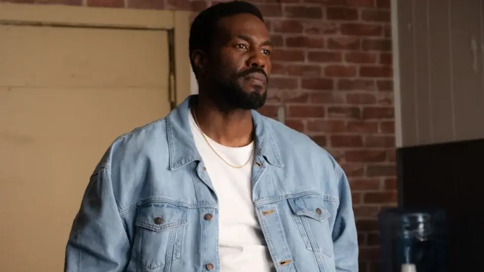 A somber Yahya Abdul-Mateen II stands in a jean jacket and white t-shirt in Wonder Man.