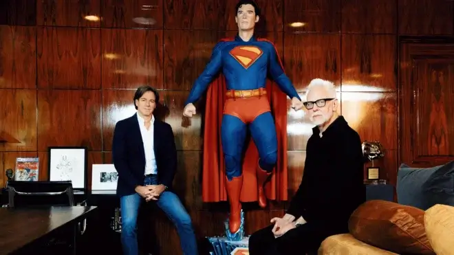 Two men sit with a Superman statue between them.